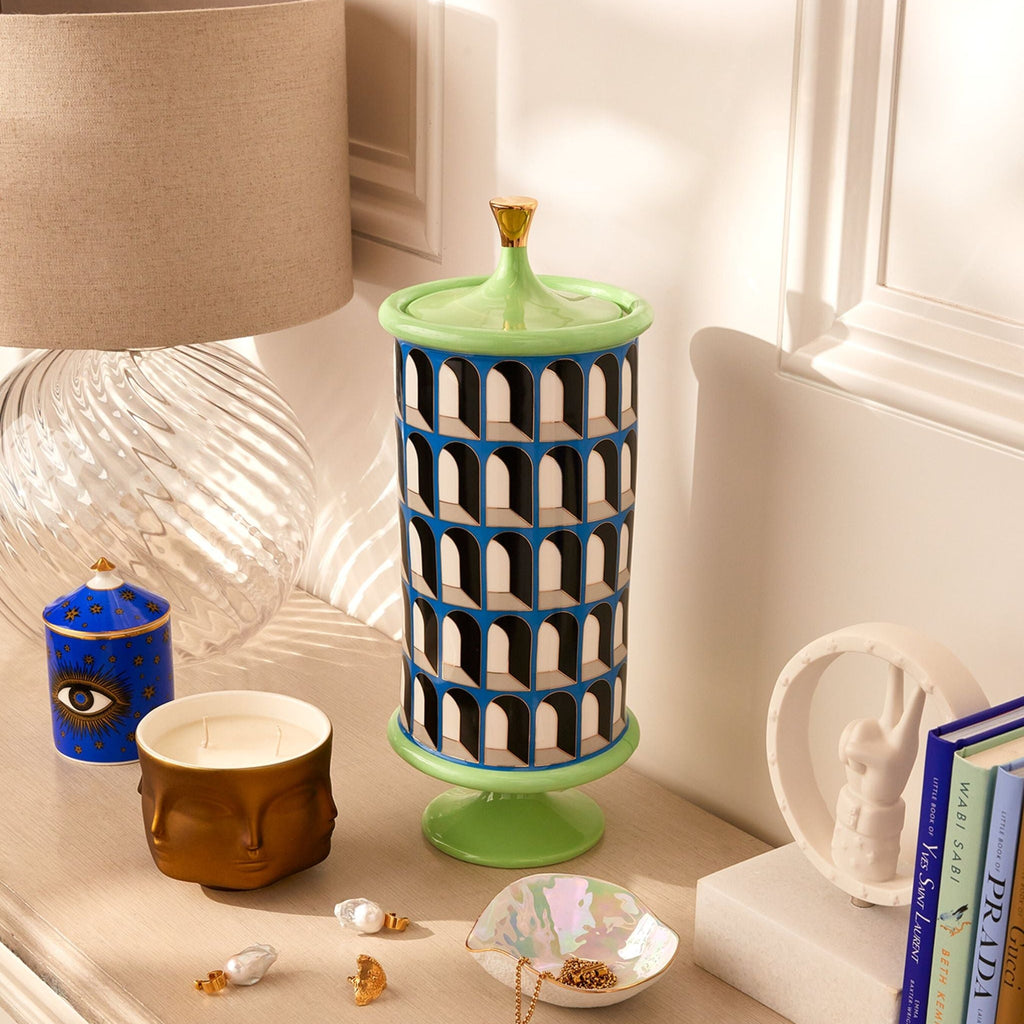 A green and blue striped canister with a geometric pattern, resembling a Colosseum, used for storage and display in a home setting.